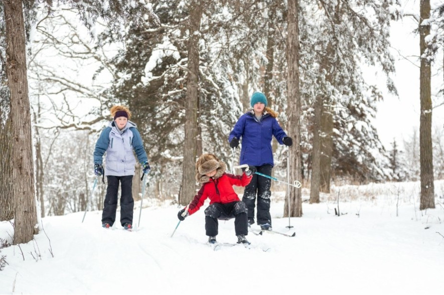 Tre barn åker längdskidor, barnet längs fram ramlar
